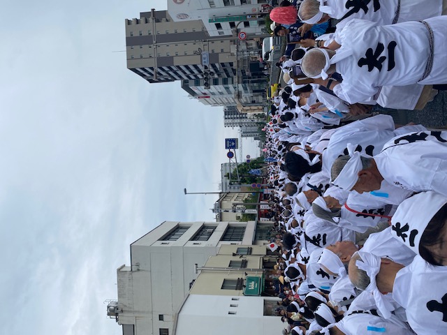 Approximately 1,000 people pull the four Tazuna poles, all wearing happi coats with the character 